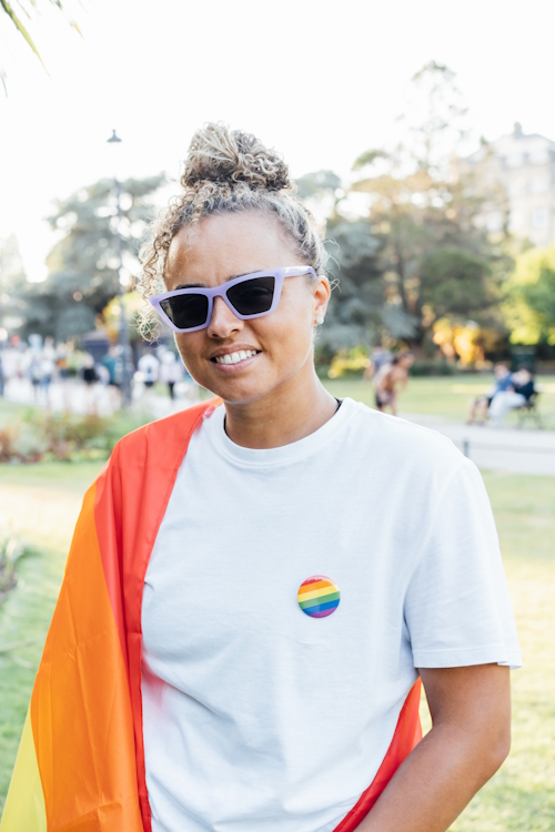 Mixed-race woman wrapped in rainbow pride flag to promote LGBTQ Inclusion in the workplace, along with promoting Diversity and Inclusion.